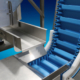 Metering hopper dispenses even product onto stainless steel vibratory feeder for gentle transport to hygienic conveyor.